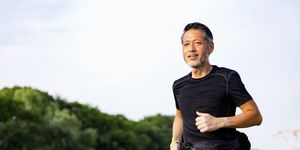 active japanese senior man jogging against the sunshine