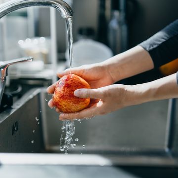 cropped shot of woman's hand washing an red apple with running water in the kitchen sink at home
