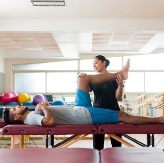 male patient lying on massage table with leg held by massage therapist, fascia stretch therapy