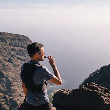 portrait of young man drinking energy sports nutrition energy gel while sitting and resting after trail running