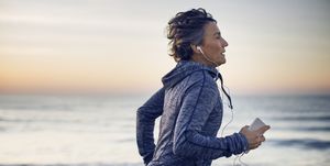 Woman jogging while listening music at beach against sky